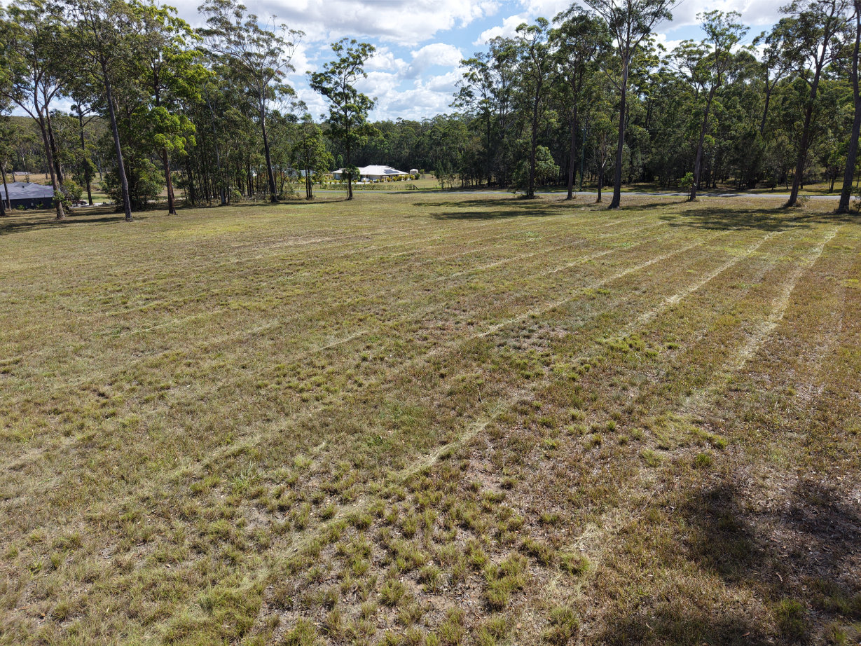 Nabiac land for sale: Scenic cleared acreage with grass, trees, and a house in the background.