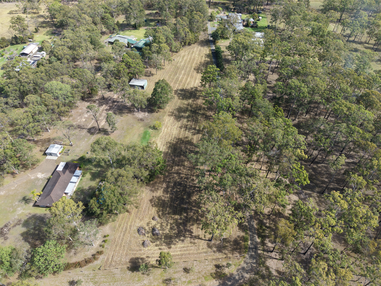Aerial view of service areas showing houses, sheds, trees, and a cleared field, showcasing property and landscape.
